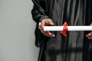 Pessoa segurando diploma de pós-graduação com fita vermelha, vestindo beca de formatura.