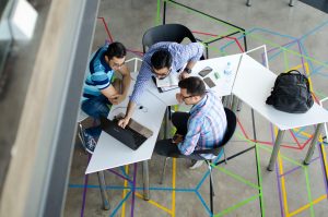 Três homens sentados ao redor de uma mesa em um ambiente moderno, colaborando em um notebook, representando um momento de networking e troca de ideias.